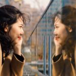 Beautiful asian girl looking at her mirror image in glass.