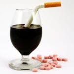 Red wine in a glass with a cigarette in it, speckled red prescription drugs on white background